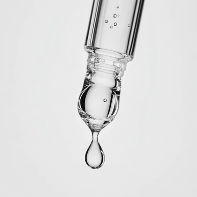 Glass dropper with a drop of liquid on a light gray background